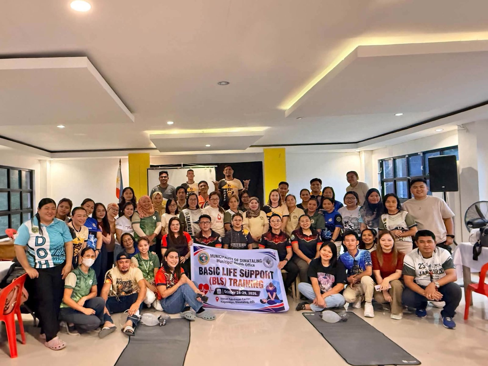 Participants and facilitators pose with a Basic Life Support training banner.