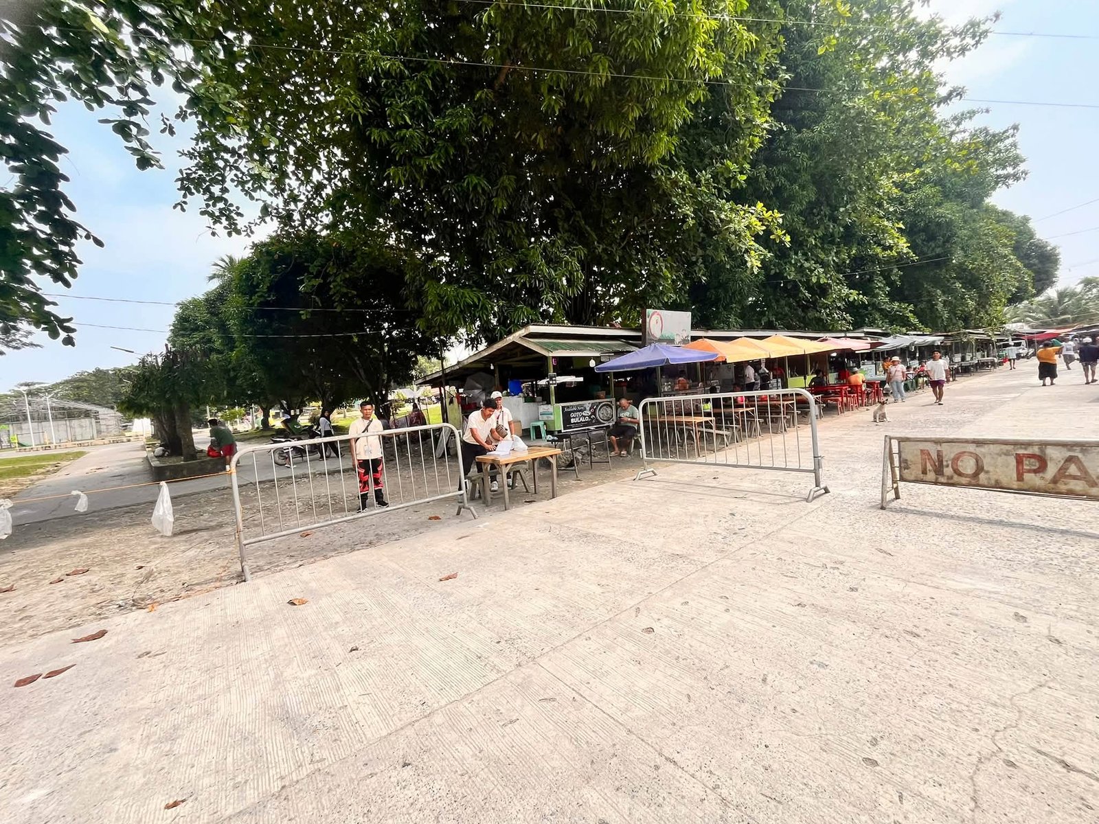 Traffic-control barriers and personnel beside roadside stalls in Dimataling.