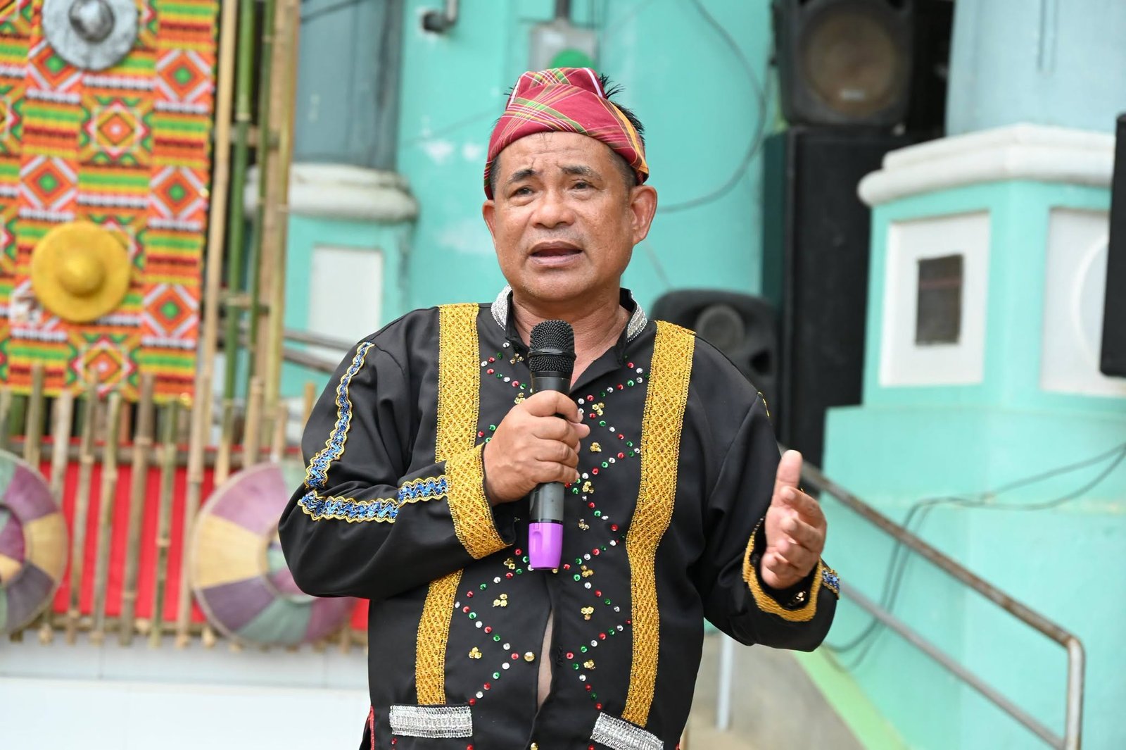 A speaker in traditional attire holds a microphone during the IP Month culmination.